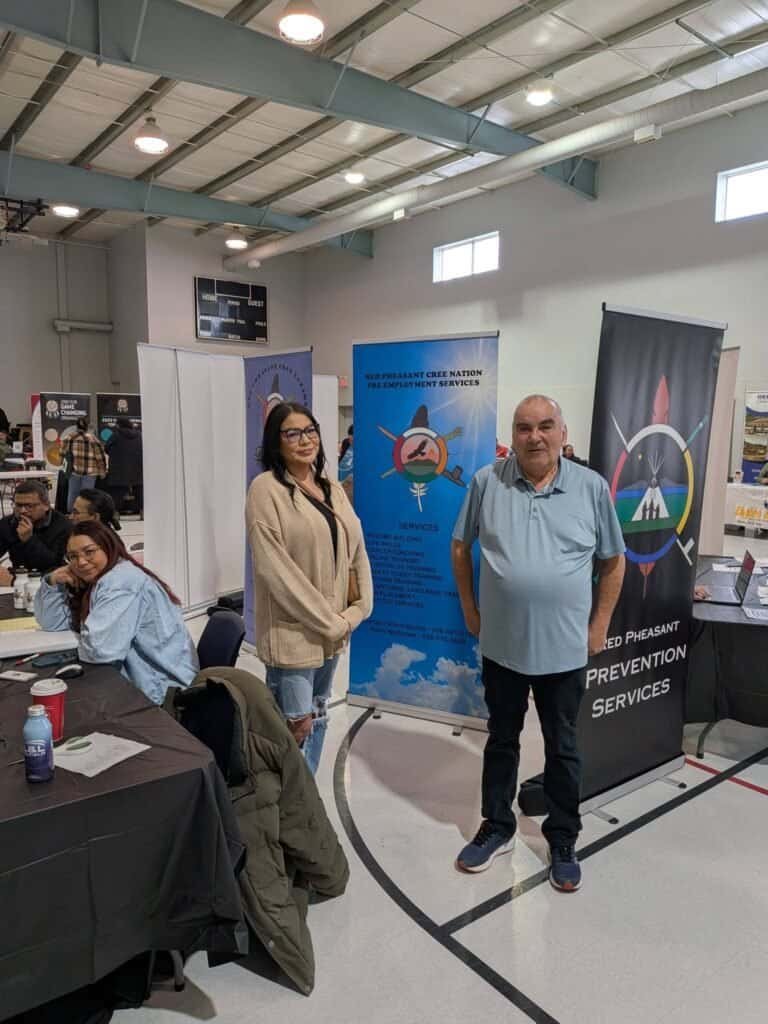 Two people standing beside the Red Pheasant Cree Nation Pre-Employment Services banner at a job fair