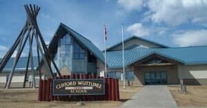 The front of Clifford Wuttunee School, with tall tipi poles and the school sign by the entrance