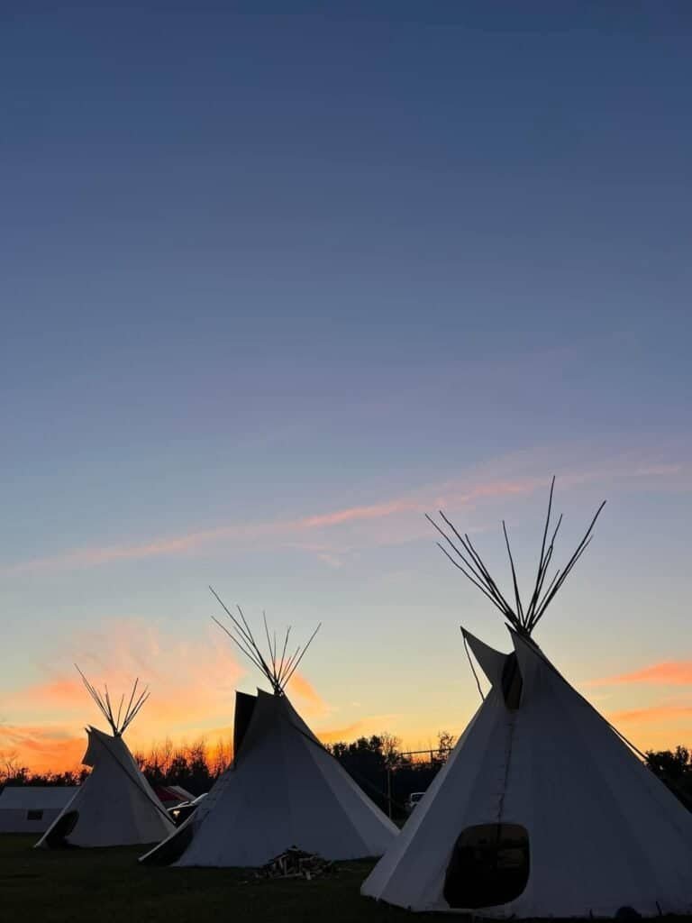 Three white tipis against an orange and blue sunset sky