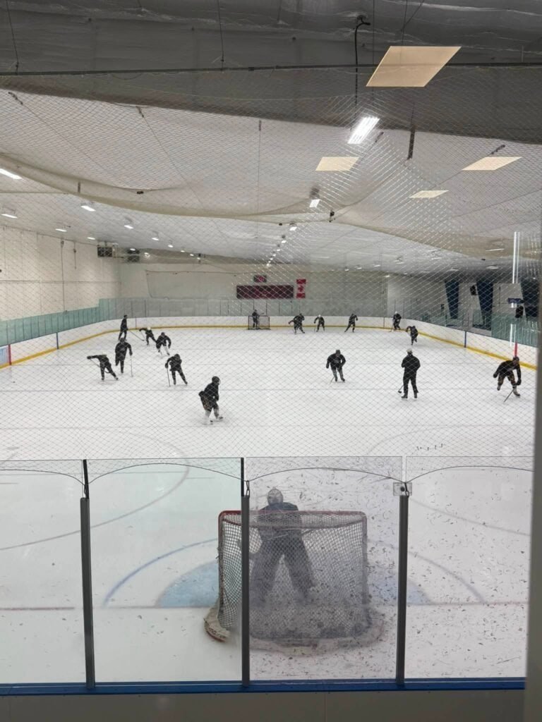 Young players in hockey gear skating drills on an indoor rink during a hockey camp